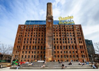 Domino Sugar Refinery building with a tall brick chimney and "Domino Sugar" sign on top.