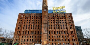 Domino Sugar Refinery building with a tall brick chimney and "Domino Sugar" sign on top.