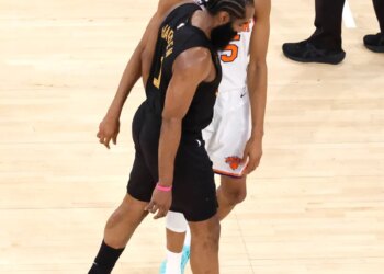 Two basketball players, one in a black jersey and one in a white jersey, standing on a court.