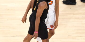 Two basketball players, one in a black jersey and one in a white jersey, standing on a court.