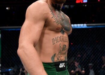 Conor McGregor stands in the octagon wearing green shorts and UFC gloves.