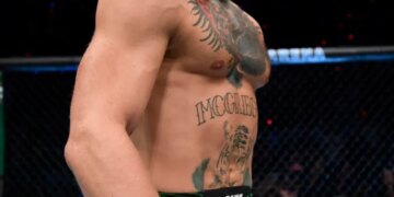 Conor McGregor stands in the octagon wearing green shorts and UFC gloves.
