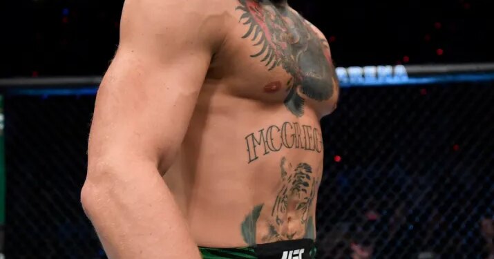 Conor McGregor stands in the octagon wearing green shorts and UFC gloves.
