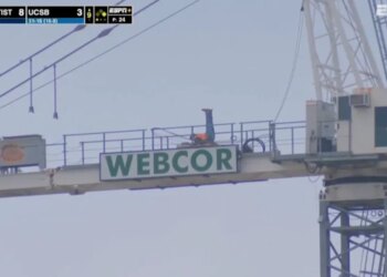A construction worker exercising on top of a Webcor sign at a Cal Baptist vs. UCSB game.