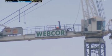 A construction worker exercising on top of a Webcor sign at a Cal Baptist vs. UCSB game.