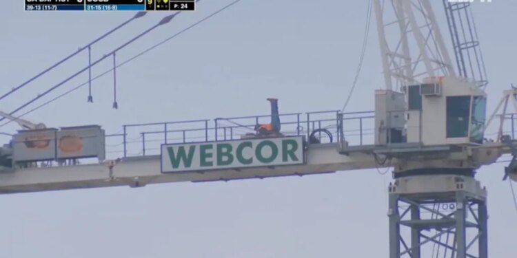 A construction worker exercising on top of a Webcor sign at a Cal Baptist vs. UCSB game.