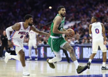 Boston Celtics player Jayson Tatum dribbles the ball down the court while being guarded by a Philadelphia 76ers player.