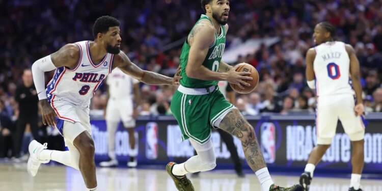 Boston Celtics player Jayson Tatum dribbles the ball down the court while being guarded by a Philadelphia 76ers player.