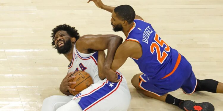 76ers center Joel Embiid (21) grimaces as he and Knicks wing Mikal Bridges (25) fight for control of the ball during Game 4 of the second round on May 10, 2026.
