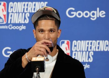 New York Knicks guard Josh Hart drinking from a wine glass at a post-game press conference.