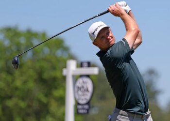 Justin Rose follows through on a golf swing, wearing a white "Morgan Stanley" cap and dark green shirt.