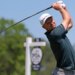 Justin Rose follows through on a golf swing, wearing a white "Morgan Stanley" cap and dark green shirt.