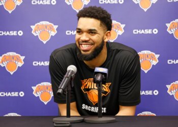 Karl-Anthony Towns smiling at a press conference with two microphones in front of him.