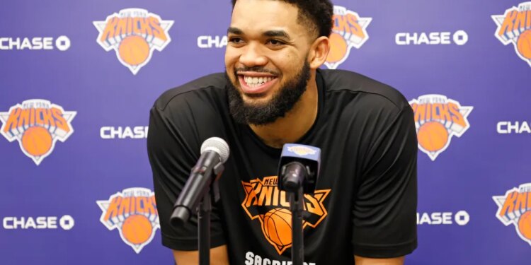 Karl-Anthony Towns smiling at a press conference with two microphones in front of him.