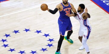 New York Knicks center Karl-Anthony Towns (32) passes the ball as Philadelphia 76ers forward Paul George (8) defends.