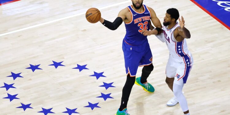 New York Knicks center Karl-Anthony Towns (32) passes the ball as Philadelphia 76ers forward Paul George (8) defends.