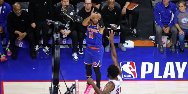 New York Knicks guard Jalen Brunson (11) shoots a three-pointer over Philadelphia 76ers center Joel Embiid (21).