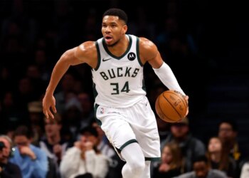 Giannis Antetokounmpo playing basketball in a white Bucks jersey with the number 34.