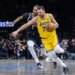 Los Angeles Lakers player in yellow jersey dribbling past a Brooklyn Nets player in black jersey.