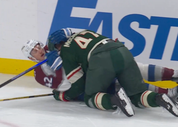 Two hockey players, one in maroon and one in green, battling for the puck on the ice.