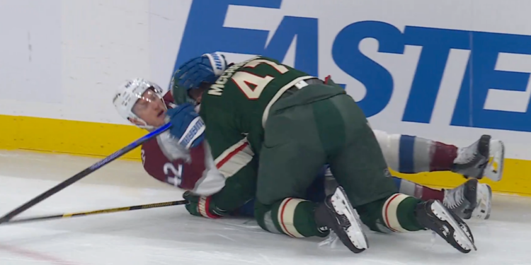 Two hockey players, one in maroon and one in green, battling for the puck on the ice.