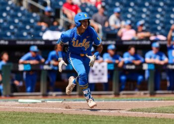 A baseball player in a blue UCLA uniform runs across the field.