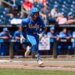 A baseball player in a blue UCLA uniform runs across the field.