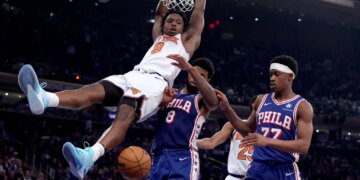 New York Knicks forward Og Anunoby #8 slams the ball over Philadelphia 76ers forward Paul George #8 and Philadelphia 76ers guard Vj Edgecombe #77 during the third quarter.