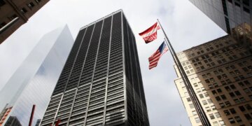 A low-angle photo looking up at tall buildings surrounding One Liberty Plaza in New York City, with an American flag and BBH flag flying between them.