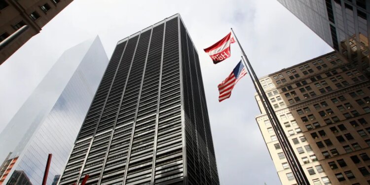 A low-angle photo looking up at tall buildings surrounding One Liberty Plaza in New York City, with an American flag and BBH flag flying between them.
