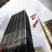 A low-angle photo looking up at tall buildings surrounding One Liberty Plaza in New York City, with an American flag and BBH flag flying between them.