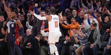 New York Knicks guard Jalen Brunson #11 celebrating a 3-point shot against the Cleveland Cavaliers, with fans cheering in the background.