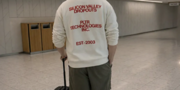 A man in a white Palantir sweatshirt that says “Silicon Valley dropouts.”