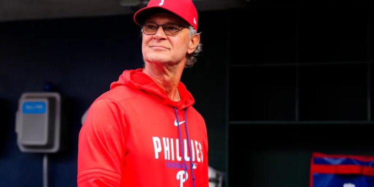 Don Mattingly in a Phillies baseball cap and red hoodie, standing in a dugout.