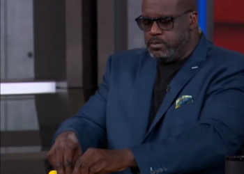Shaquille O'Neal holding up tiny red and yellow shoes.