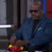 Shaquille O'Neal holding up tiny red and yellow shoes.