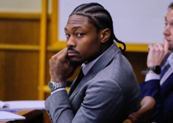 Former Patriots wide receiver Stefon Diggs in court, wearing a suit and cornrows, looking directly at the camera with his hand on his chin.