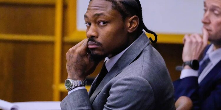 Former Patriots wide receiver Stefon Diggs in court, wearing a suit and cornrows, looking directly at the camera with his hand on his chin.
