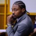 Former Patriots wide receiver Stefon Diggs in court, wearing a suit and cornrows, looking directly at the camera with his hand on his chin.