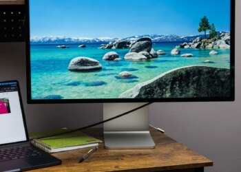 The Apple Studio Display on a small wooden desk with a MacBook Air next to it.