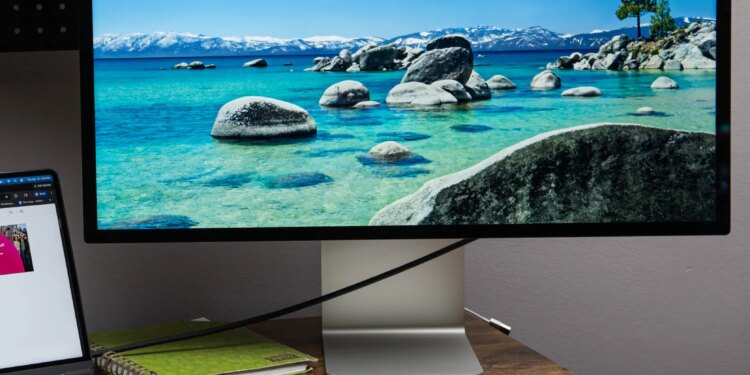 The Apple Studio Display on a small wooden desk with a MacBook Air next to it.