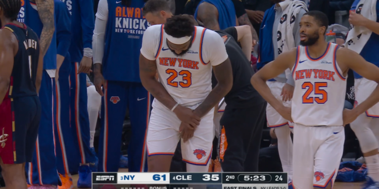 Mitchell Robinson, in a white New York Knicks jersey, clutches his right hand in pain.