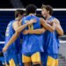 Four male volleyball players in blue and gold jerseys huddle together, arms around each other.