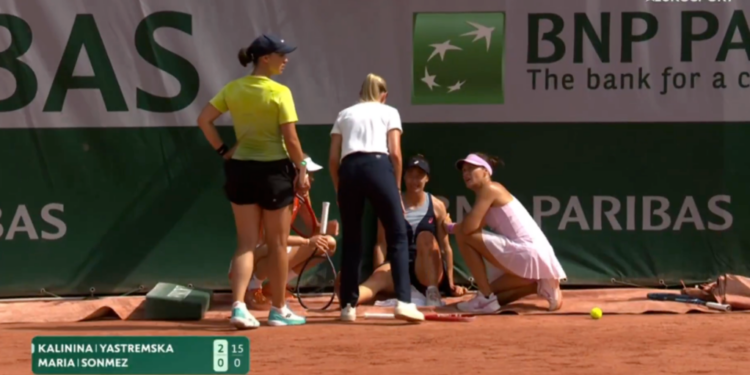 Two tennis players, a referee, and a trainer on a clay court with a score graphic for Kalinina and Yastremska.