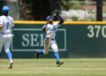 A baseball player in a UCLA uniform catches a fly ball in the outfield.