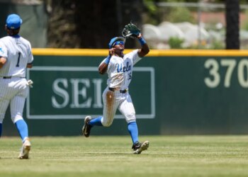 A baseball player in a UCLA uniform catches a fly ball in the outfield.
