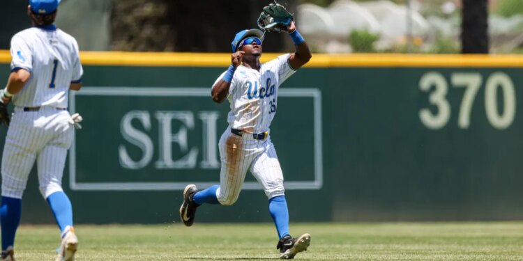 A baseball player in a UCLA uniform catches a fly ball in the outfield.