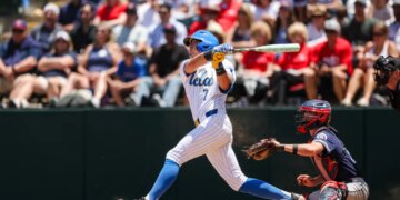 Roman Martin of UCLA batting a baseball with a catcher behind him.
