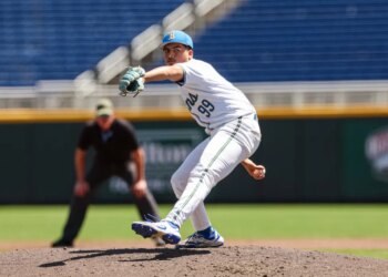 A baseball pitcher in a white uniform with blue and yellow accents pitches from a mound.
