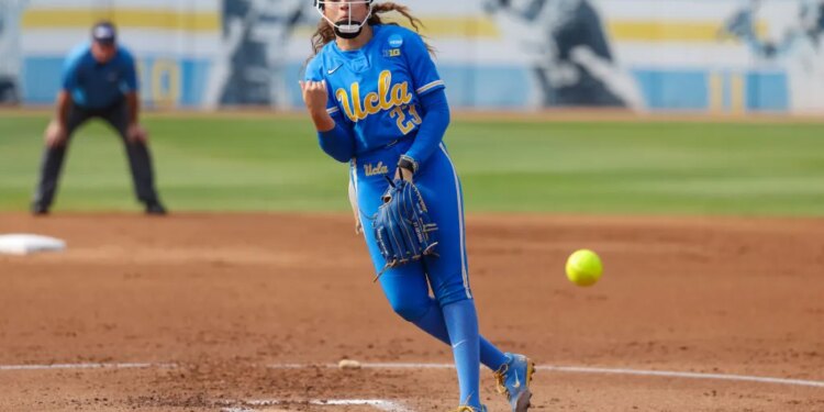 A UCLA softball pitcher in a blue uniform with yellow lettering pitches a neon yellow softball.